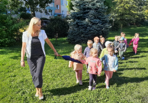 Dzieci spacerują po ogrodzie, trzymają się węża spacerowego